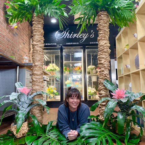 One of our employees poses between two tall artificial palms, near the Shirley's cooler